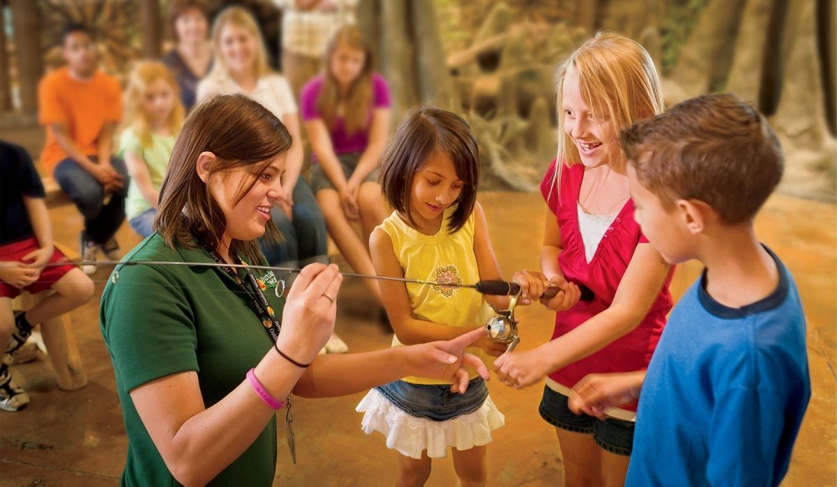 Person teaching a group of children how to use a fishing rod