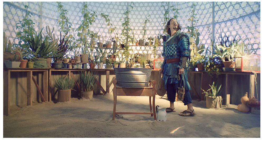 screenshot of CHRONOS, TIME OF SAND by Nicole Dextras showing a man in a layered costume, in a greenhouse with sand on the floor. He is looking at the ceiling in awe.